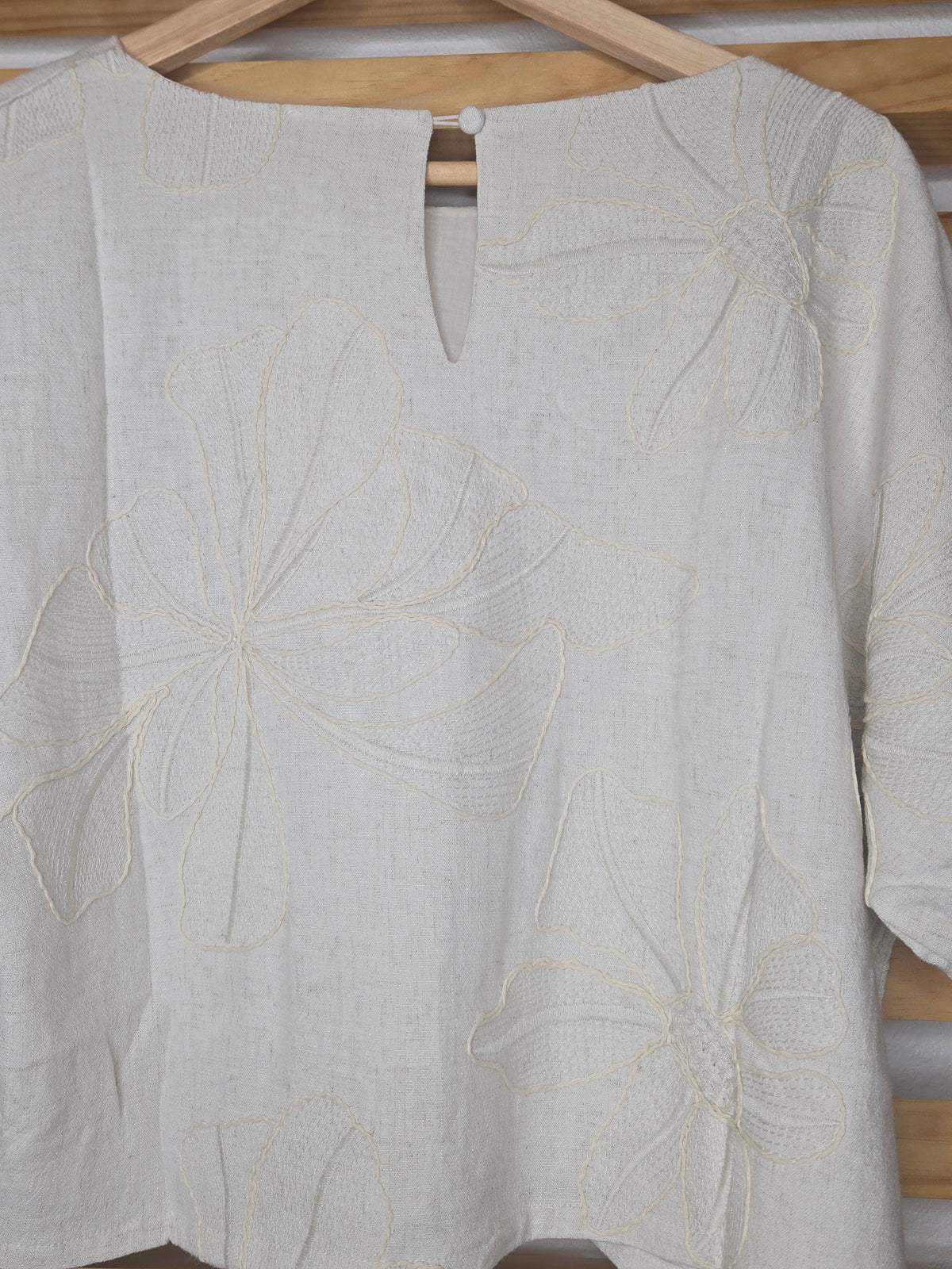Beige linen-blend top with floral embroidery, featuring short dolman sleeves with elastic cuffs and a soft inner lining
