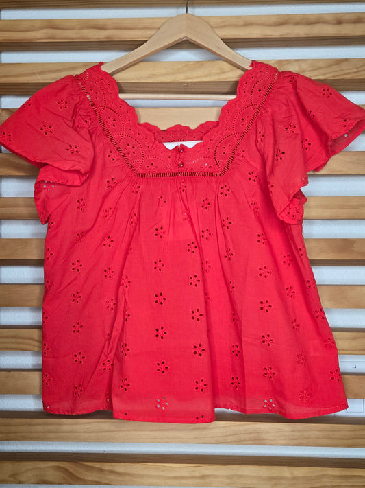 Red blouse with floral cut-out details on a wooden hanger against a wooden panel background