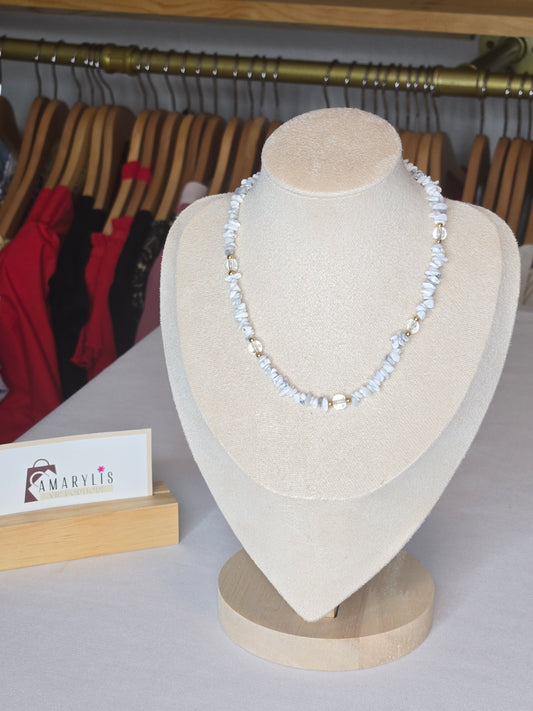 A delicate white beaded necklace with clear faceted beads displayed on a beige jewelry bust. The bust is set against a background showing clothing racks and a small sign with the brand name 'MARVIS'.
