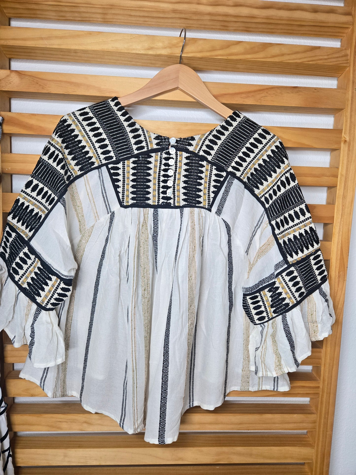V-neck blouse with black embroidery details, flutter sleeves, and vertical stitched accents for a flattering silhouette.