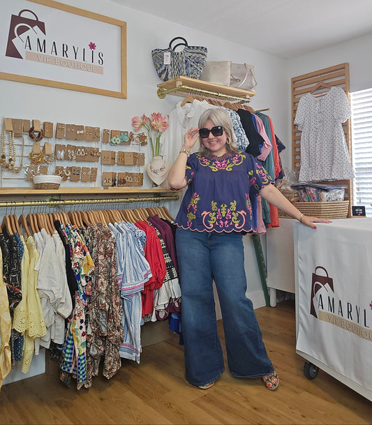 Woman wearing a navy short sleeve blouse with colorful embroidery details and scalloped trim accents in pink and green.