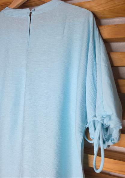 A light blue women's blouse with a round neckline, pleated details, short sleeves, and adjustable tie cuffs.