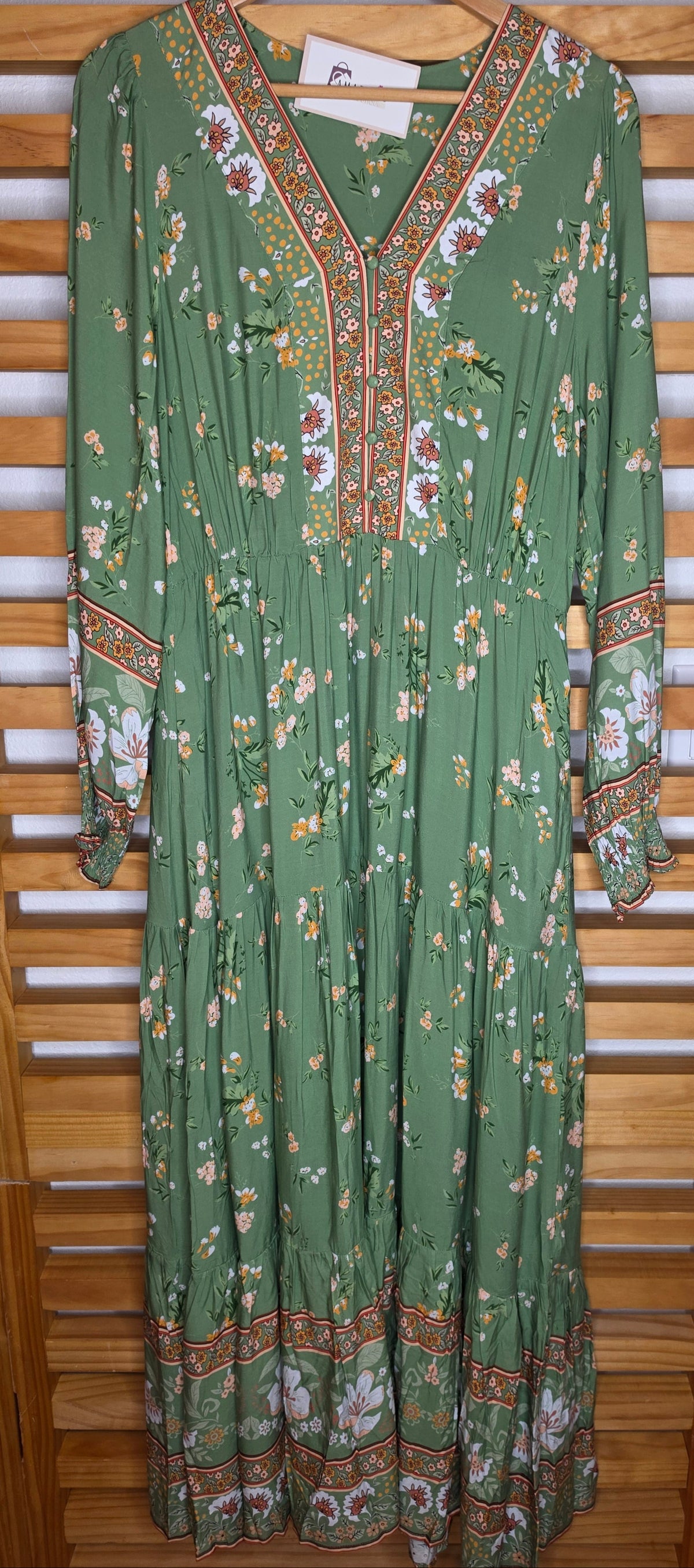 Floral print maxi dress featuring a contrasting border print, split V-neckline, button-front bodice, elastic empire waist, long sleeves with smocked cuffs, and tiered skirt.