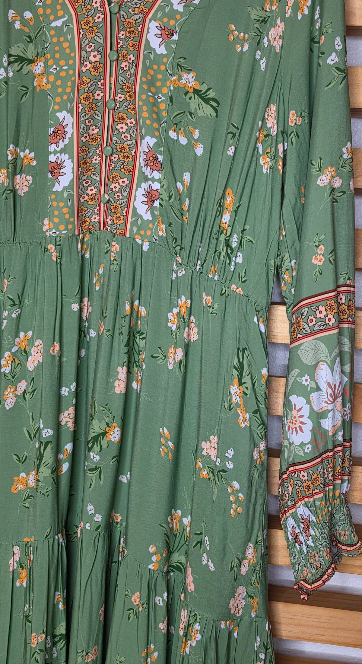 Floral print maxi dress featuring a contrasting border print, split V-neckline, button-front bodice, elastic empire waist, long sleeves with smocked cuffs, and tiered skirt.