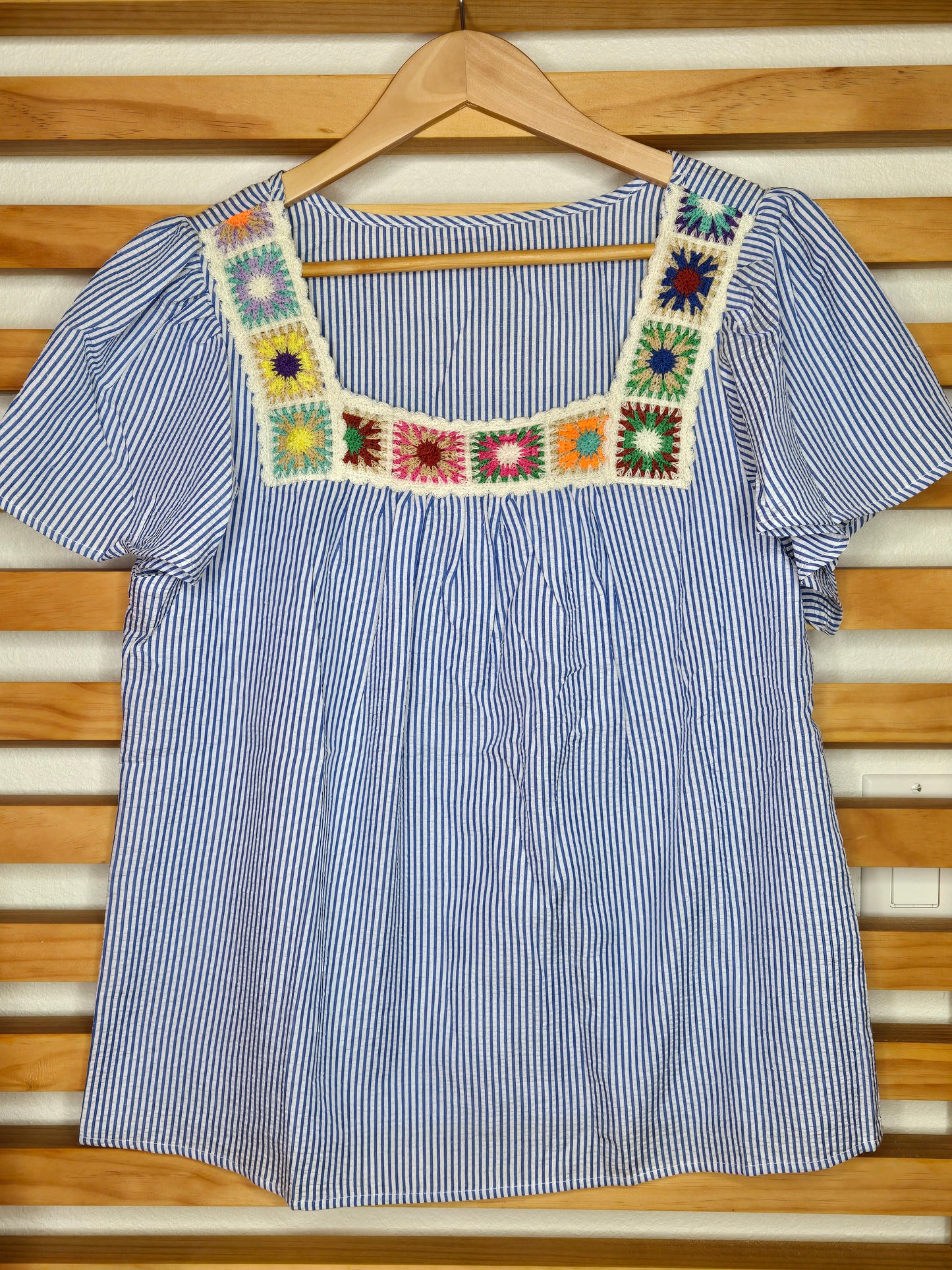 Blue and white striped shirt with colorful crochet trim on a wooden hanger. amarylisvipboutique