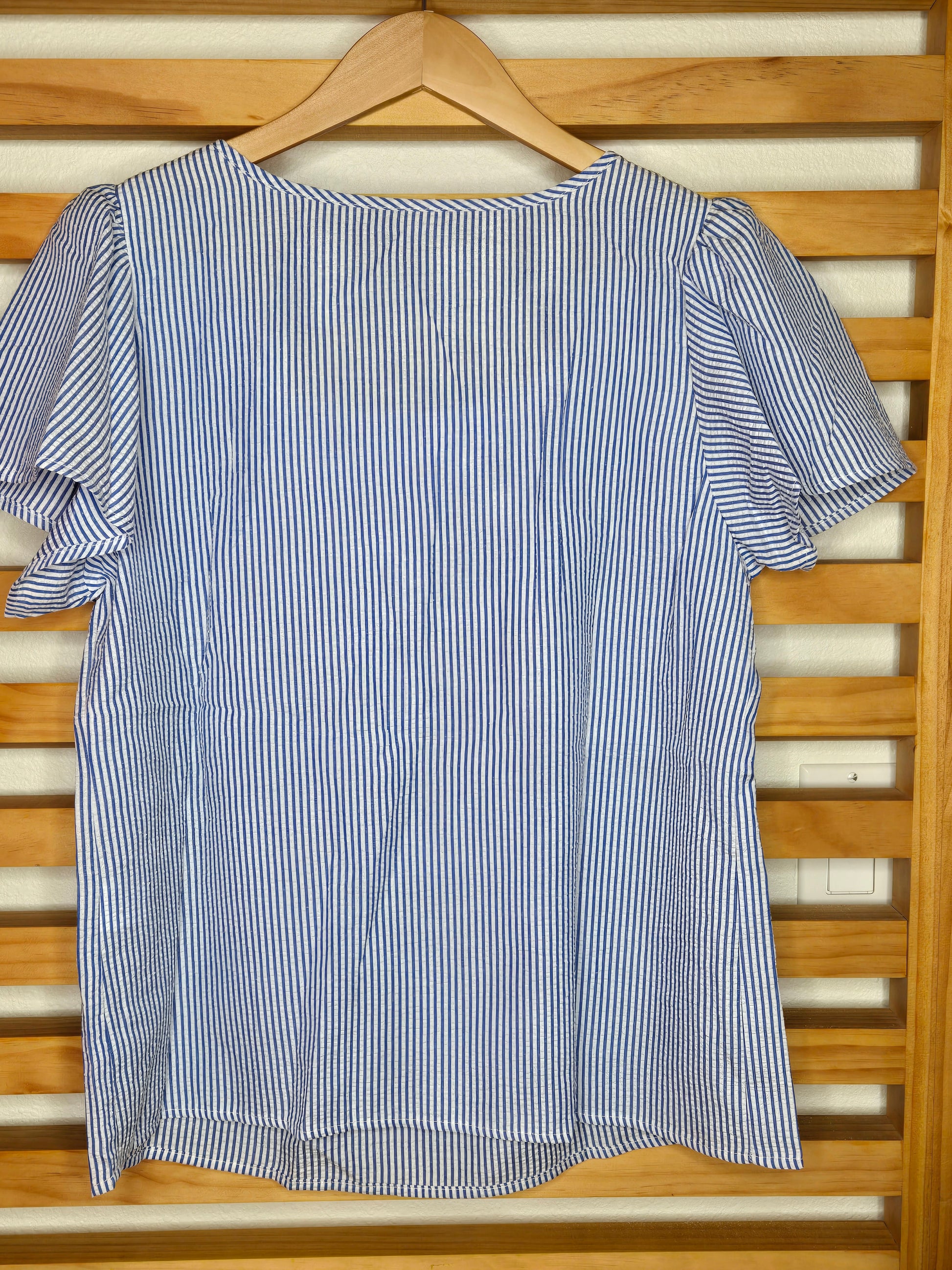Blue and white striped shirt on a wooden hanger against a wooden background