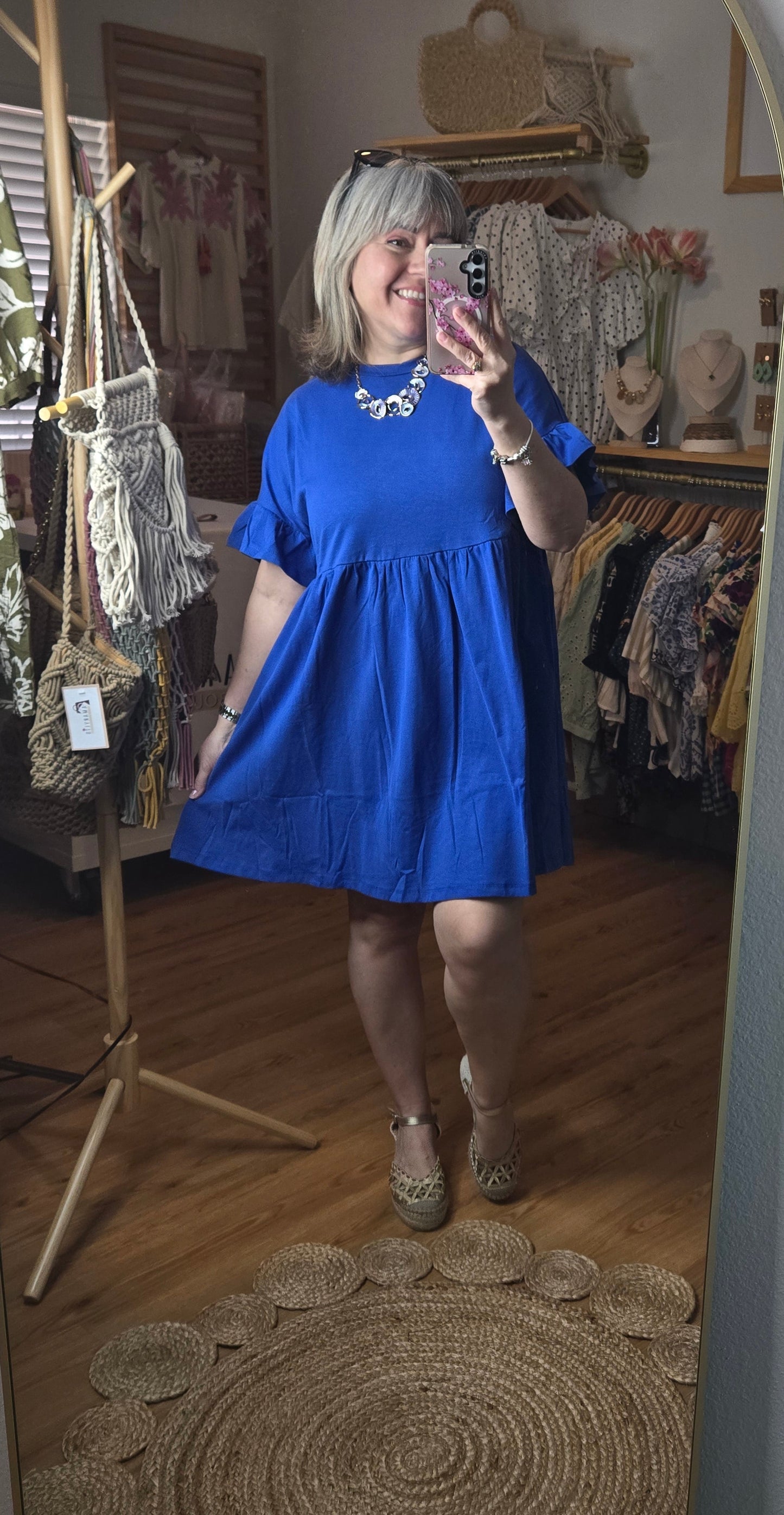 Short blue cotton dress with round neckline, drop shoulders, short ruffle sleeves, and ruffle hem in a relaxed fit design.