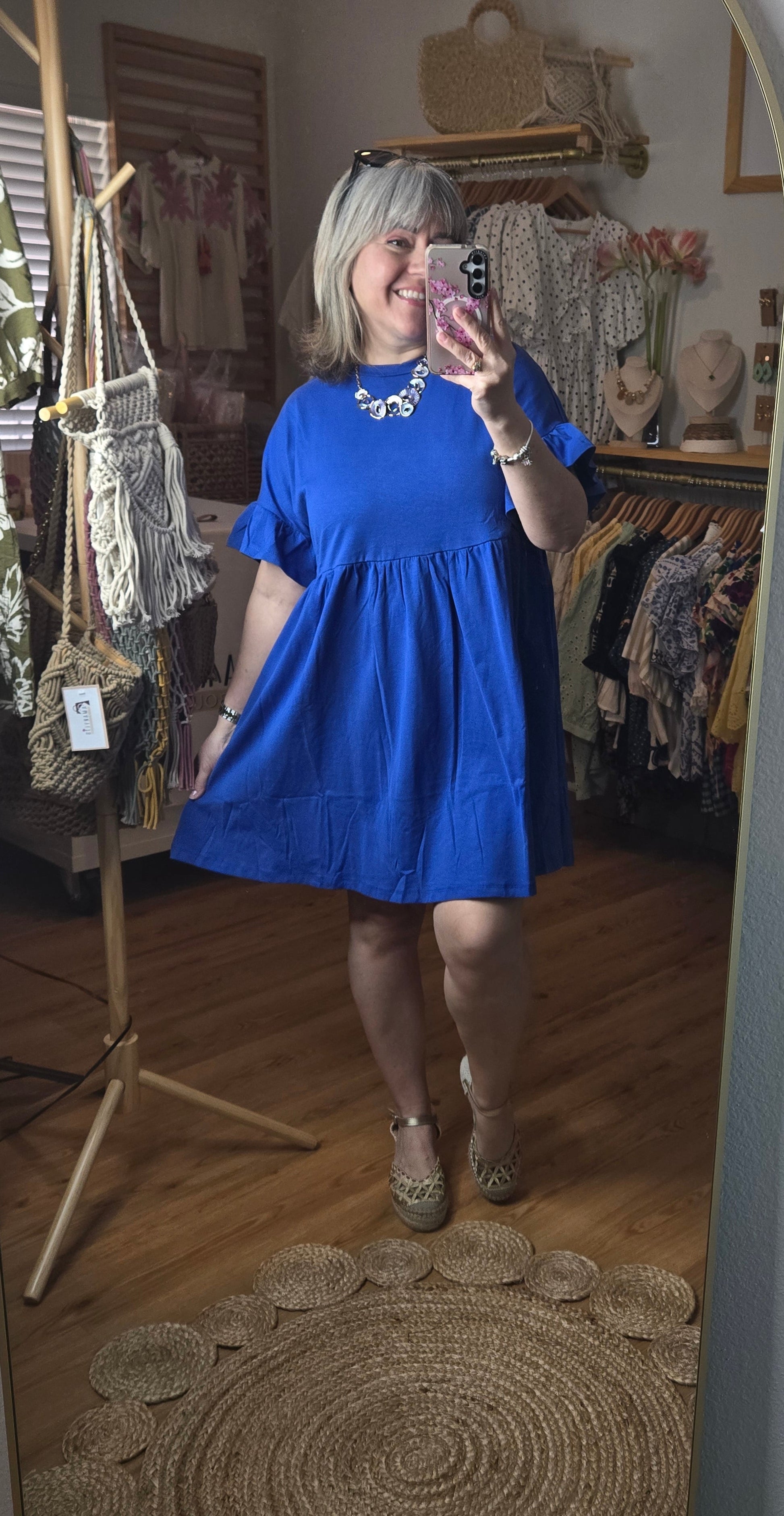 Short blue cotton dress with round neckline, drop shoulders, short ruffle sleeves, and ruffle hem in a relaxed fit design.