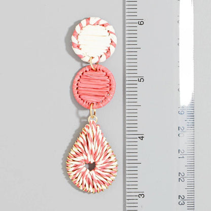 Pink and white raffia earrings with a ruler for scale on a gray background