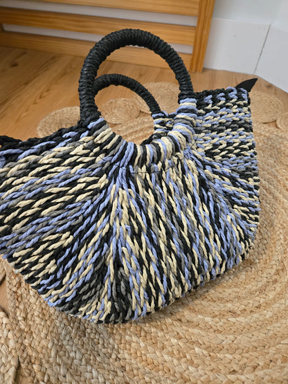 Straw tote bag with a subtle sheen, featuring a multi-tone woven design, distinctive half-moon round handles, a secure zipper closure, and an adjustable strap for crossbody wear. A versatile, timeless piece with a refined yet relaxed style.