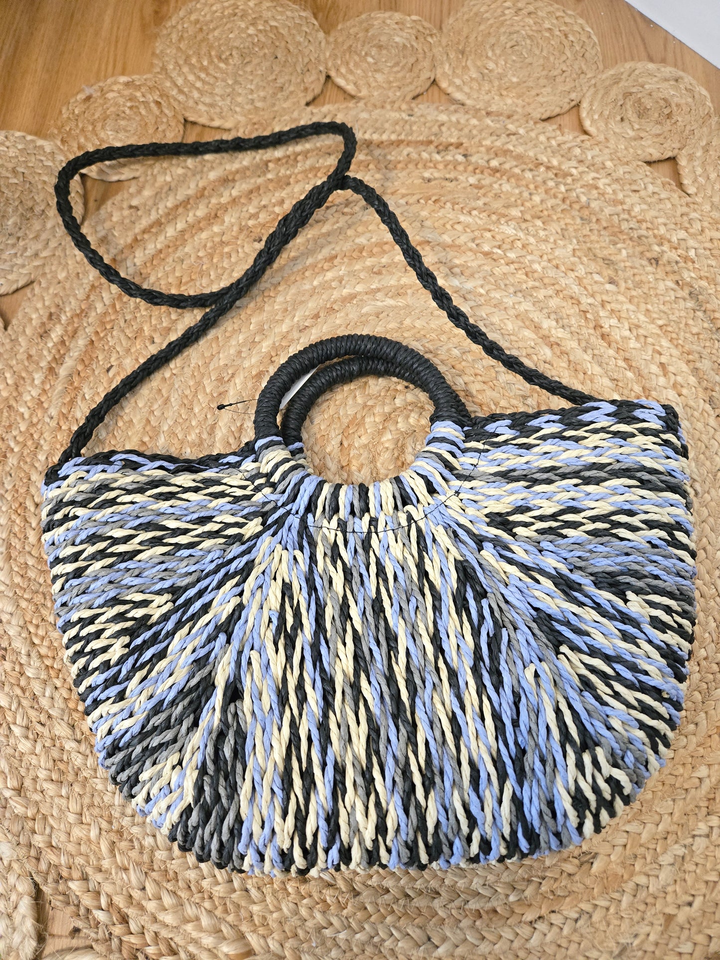Straw tote bag with a subtle sheen, featuring a multi-tone woven design, distinctive half-moon round handles, a secure zipper closure, and an adjustable strap for crossbody wear. A versatile, timeless piece with a refined yet relaxed style.