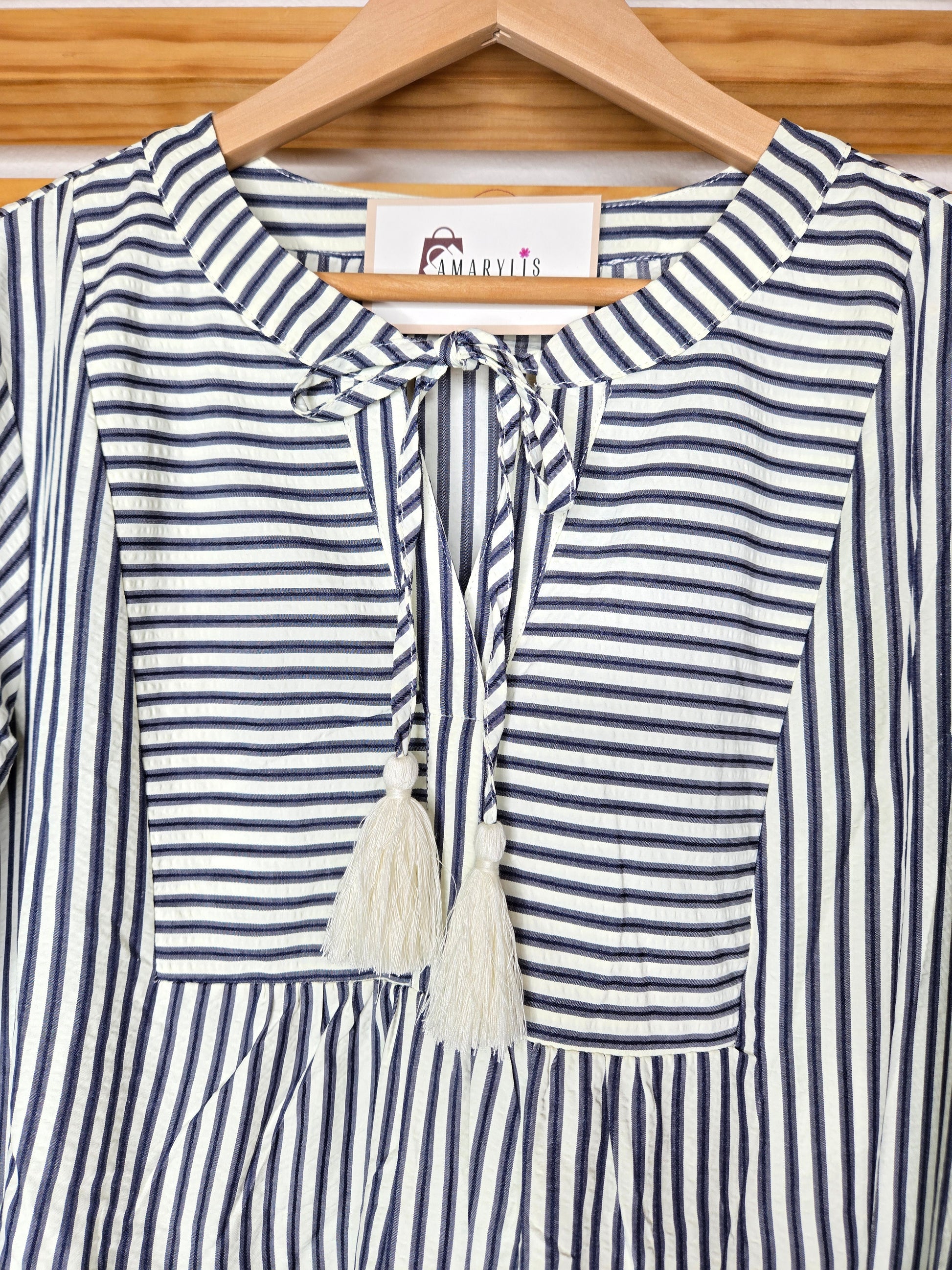 Navy striped cotton babydoll dress with bell sleeves, tassel tie neckline, relaxed fit silhouette, and functional side pockets.