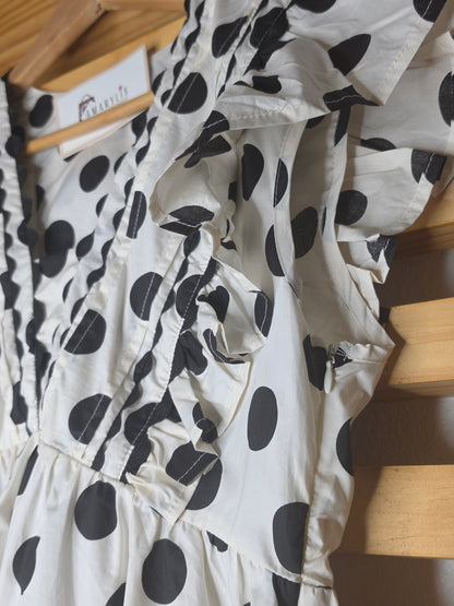 Black and white polka dot babydoll blouse with ruffle details, fitted bust, relaxed lower silhouette, and side zipper.