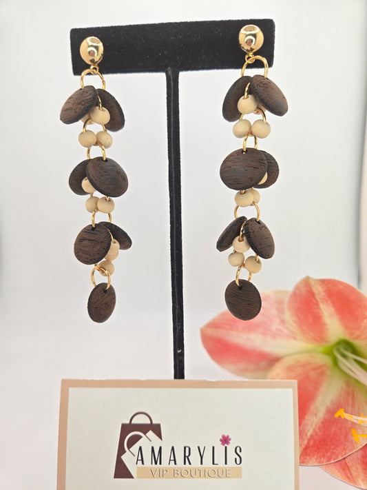 A pair of dangling earrings displayed on a black T-stand. Each earring has gold-tone studs and hooks with layered dark brown wooden discs and small cream-colored beads.