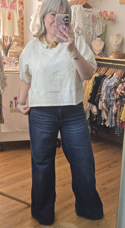 Beige linen-blend top with floral embroidery, featuring short dolman sleeves with elastic cuffs and a soft inner lining