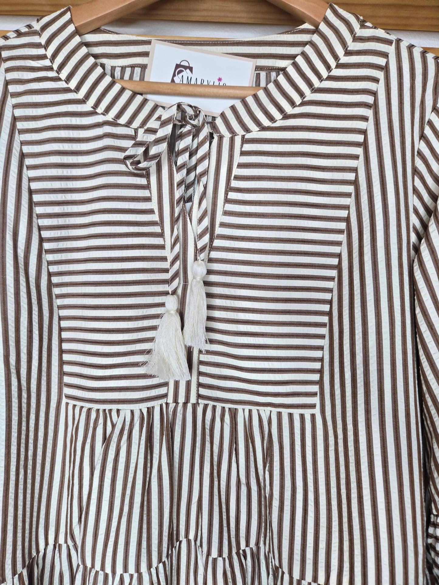 Lightweight cotton dress featuring classic color chocolate stripes, flowy bell sleeves, and a tassel tie neckline for a relaxed boho-inspired look. The loose silhouette offers comfort and movement, while the side pockets add everyday practicality. A charming and feminine piece that’s perfect for casual days or relaxed outings