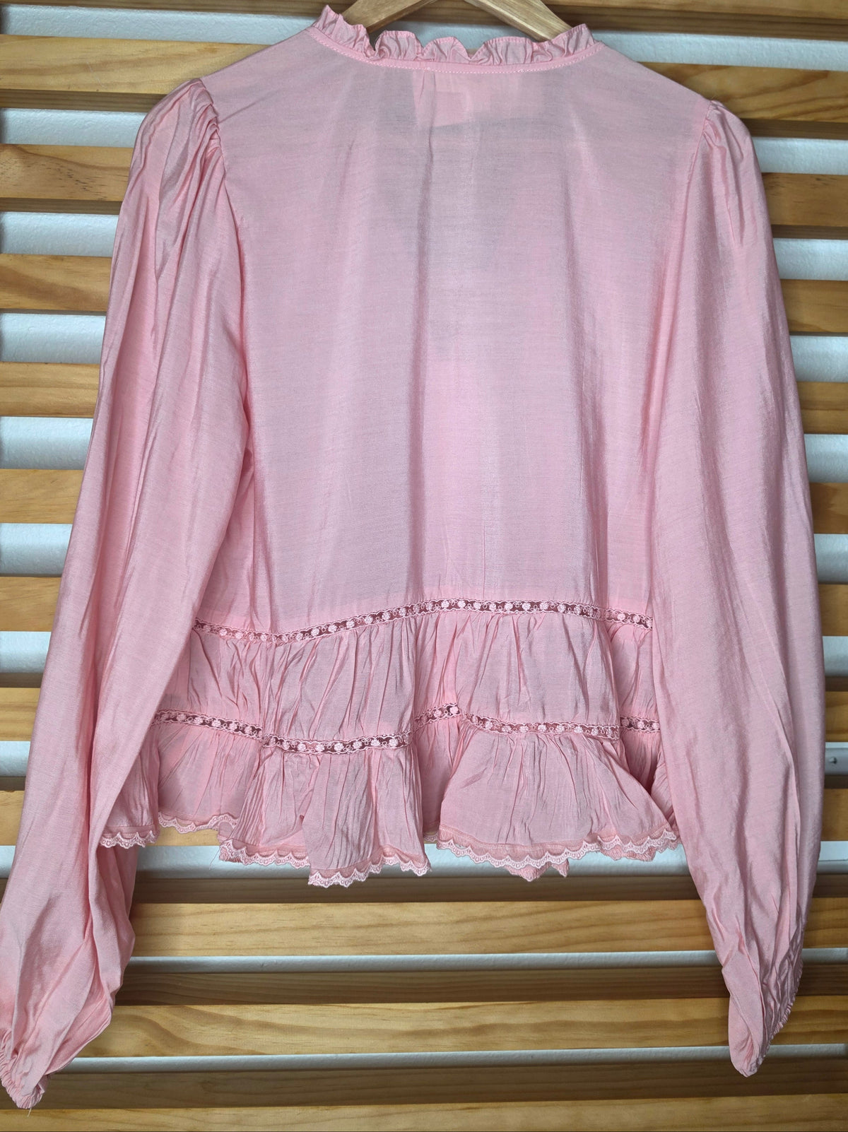 Women’s white blouse with V-neckline, button front, lace-trimmed ruffles, delicate pin-tuck details, and long balloon sleeves with elastic cuffs.