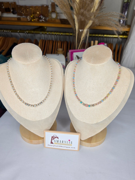 Two beaded necklaces displayed on cream-colored fabric mannequin busts. The necklace on the left is made of small clear faceted beads, while the necklace on the right features pastel pink, blue, and orange beads.