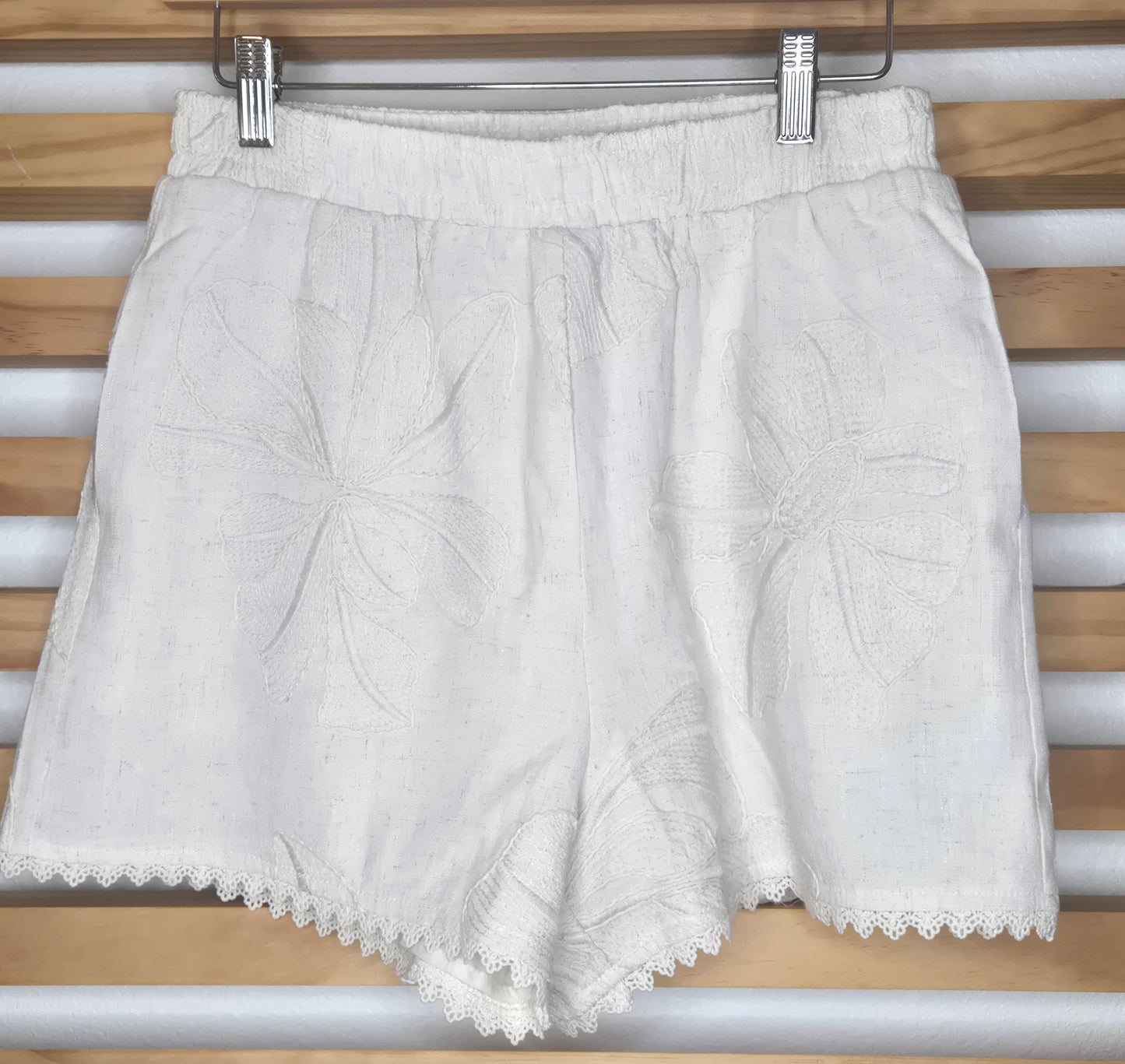 Beige embroidered shorts featuring delicate floral embroidery, crochet lace trim, side pockets, and a comfortable elastic waistband. Styled with the matching embroidered top, sold separately.