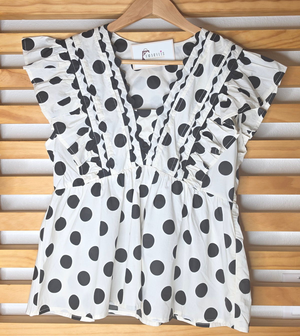 Black and white polka dot babydoll blouse with ruffle details, fitted bust, relaxed lower silhouette, and side zipper.