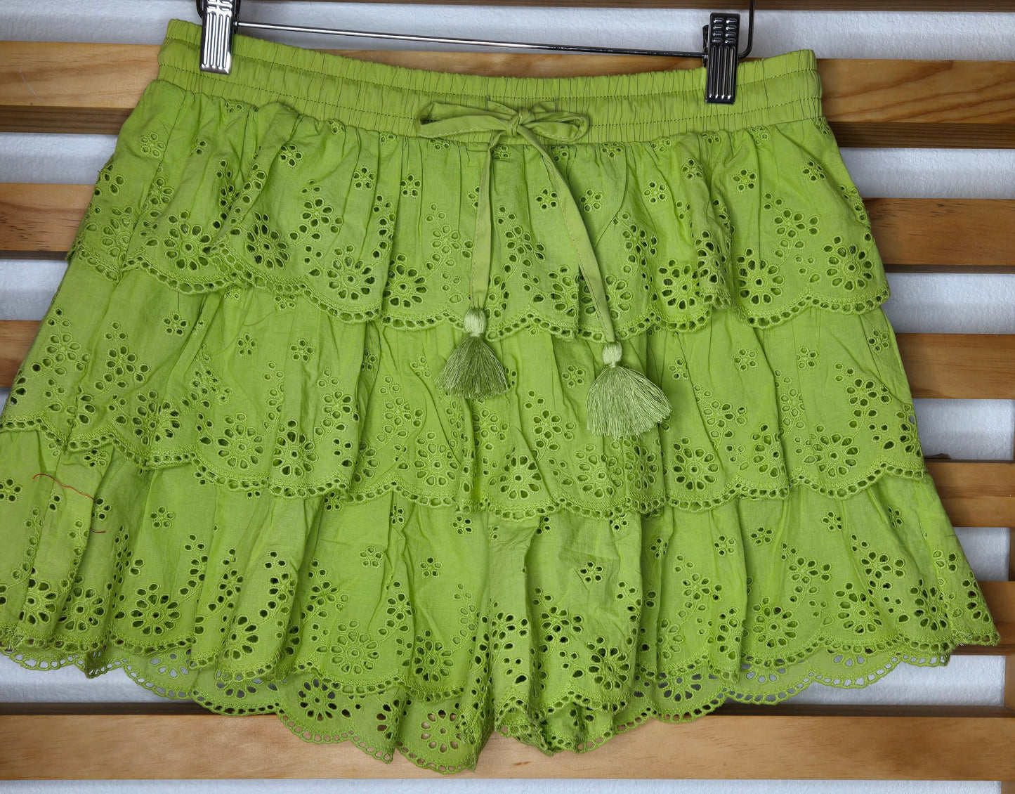 Women's eyelet shorts featuring a tiered ruffle design, elastic waistband, and adjustable tassel drawstring, available in green and white.