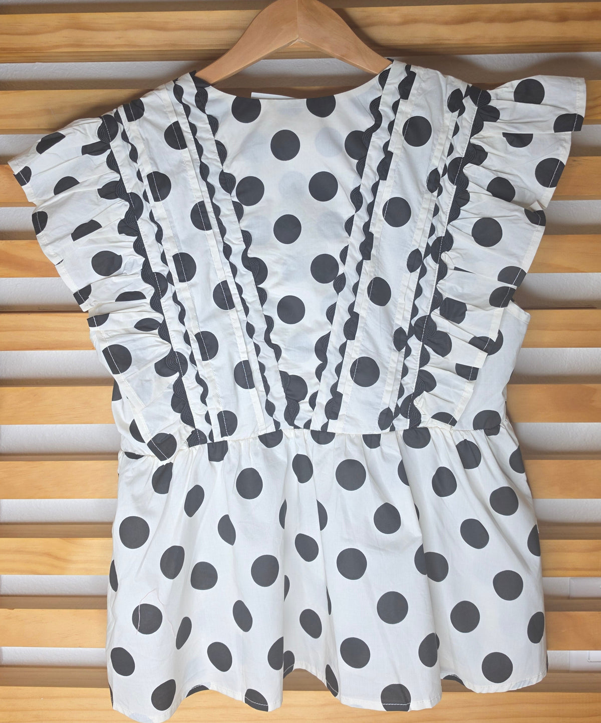 Black and white polka dot babydoll blouse with ruffle details, fitted bust, relaxed lower silhouette, and side zipper.