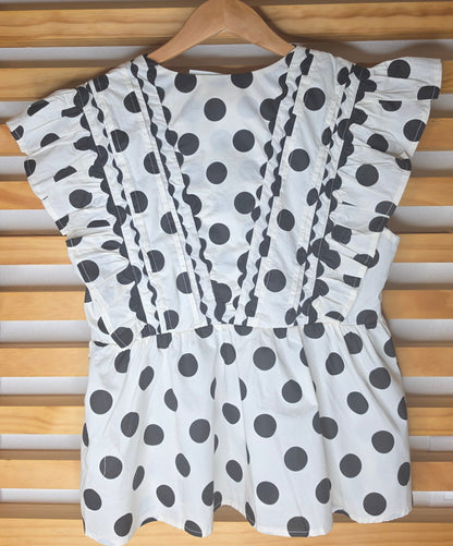 Black and white polka dot babydoll blouse with ruffle details, fitted bust, relaxed lower silhouette, and side zipper.