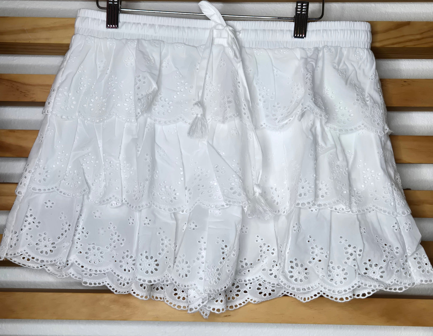 Women's eyelet shorts featuring a tiered ruffle design, elastic waistband, and adjustable tassel drawstring, available in green and white.