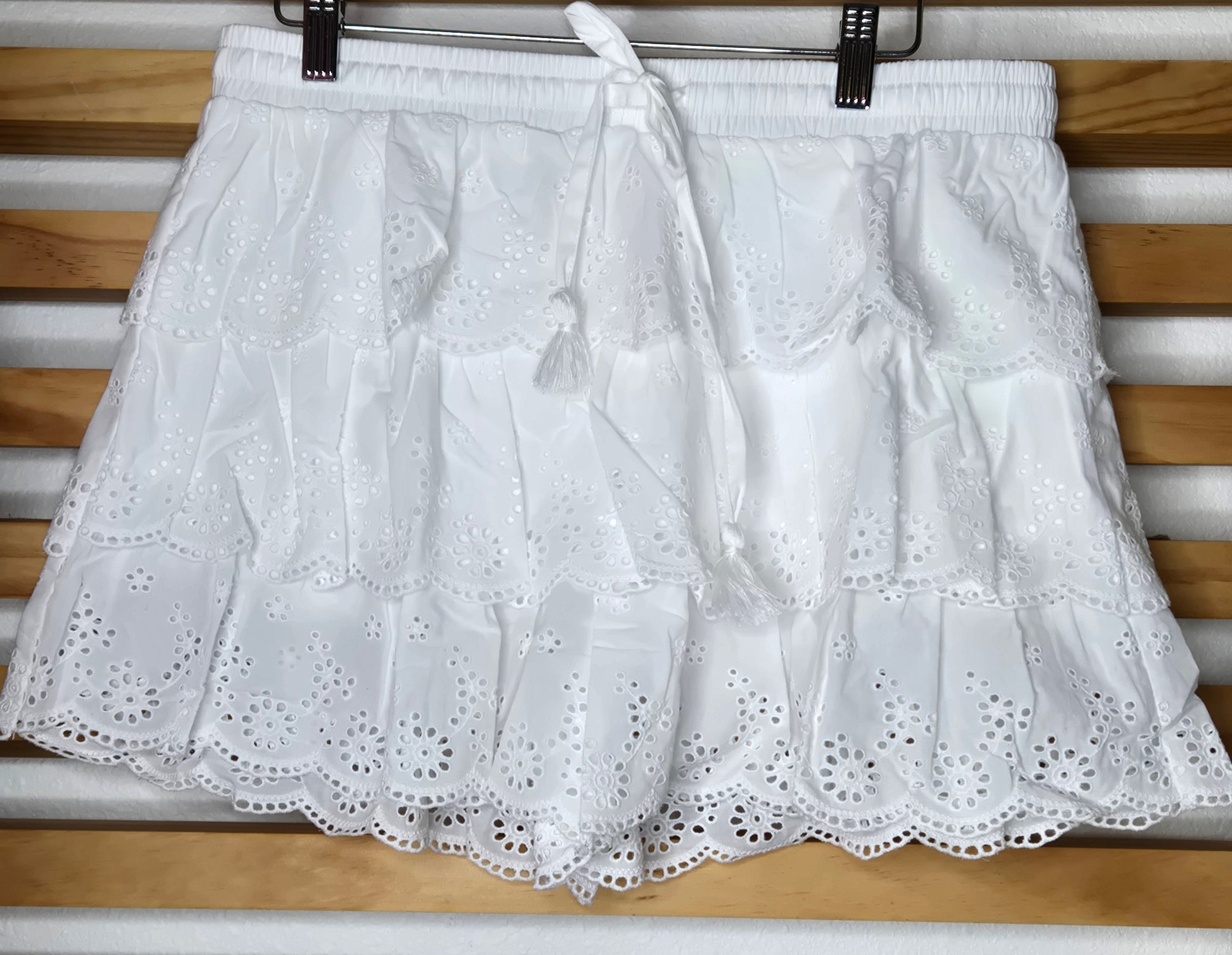 Women's eyelet shorts featuring a tiered ruffle design, elastic waistband, and adjustable tassel drawstring, available in green and white.