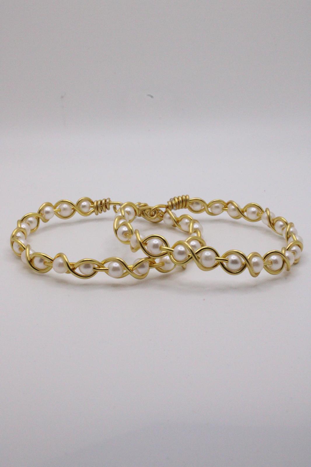 A gold-tone jewelry set with white faux pearls, including a bracelet and matching earrings, displayed on a black stand with a branded card below on a light gray background.