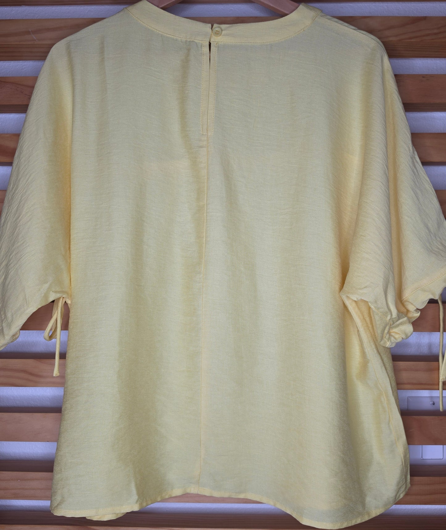 A yellow women's blouse with a round neckline, pleated details, short sleeves, and adjustable tie cuffs.