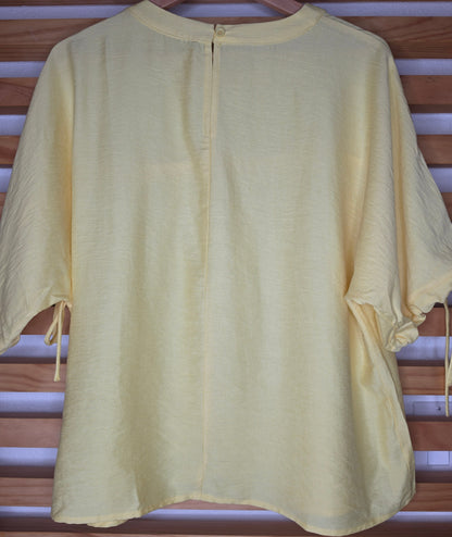 A yellow women's blouse with a round neckline, pleated details, short sleeves, and adjustable tie cuffs.