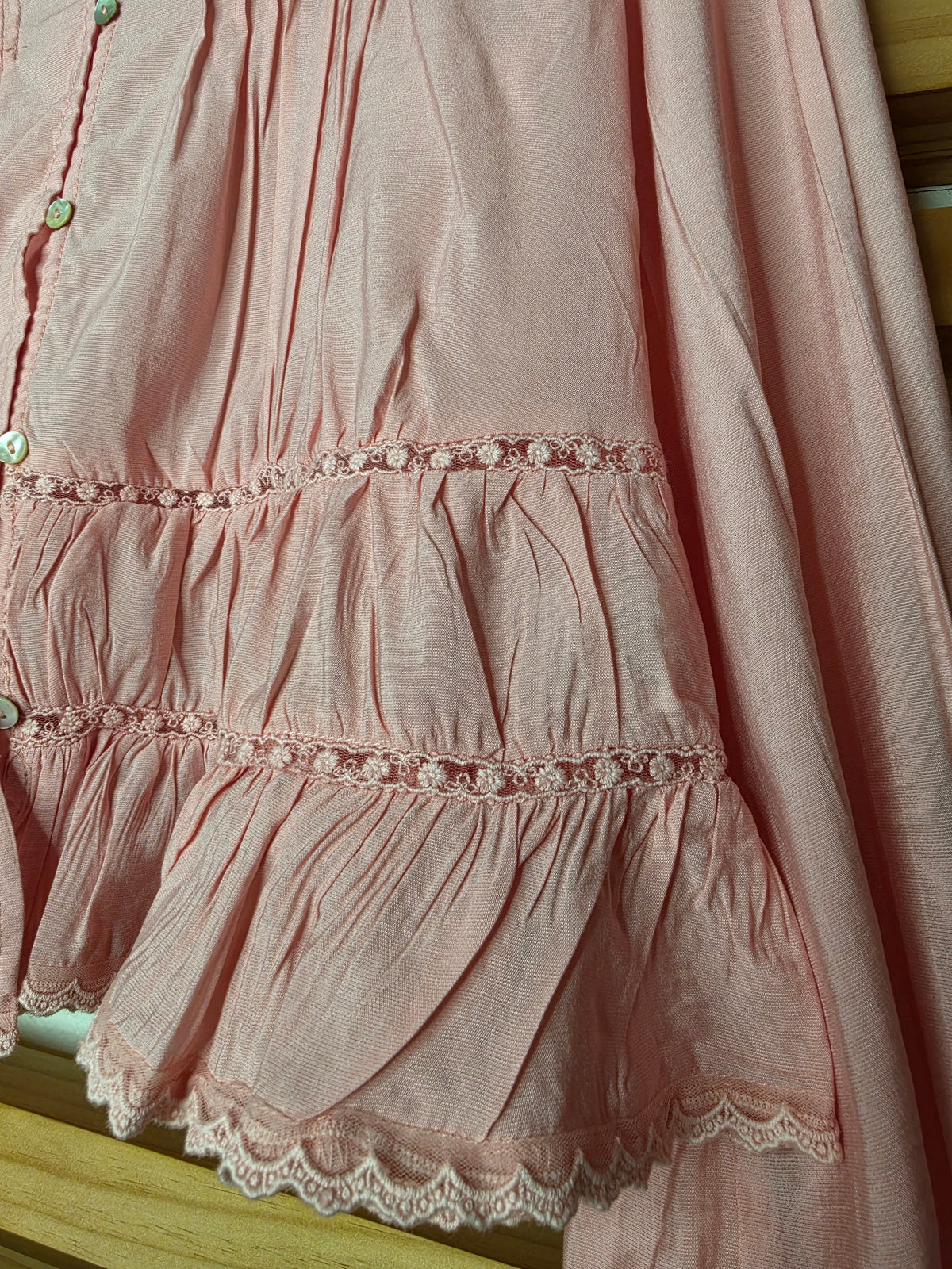 Women’s white blouse with V-neckline, button front, lace-trimmed ruffles, delicate pin-tuck details, and long balloon sleeves with elastic cuffs.