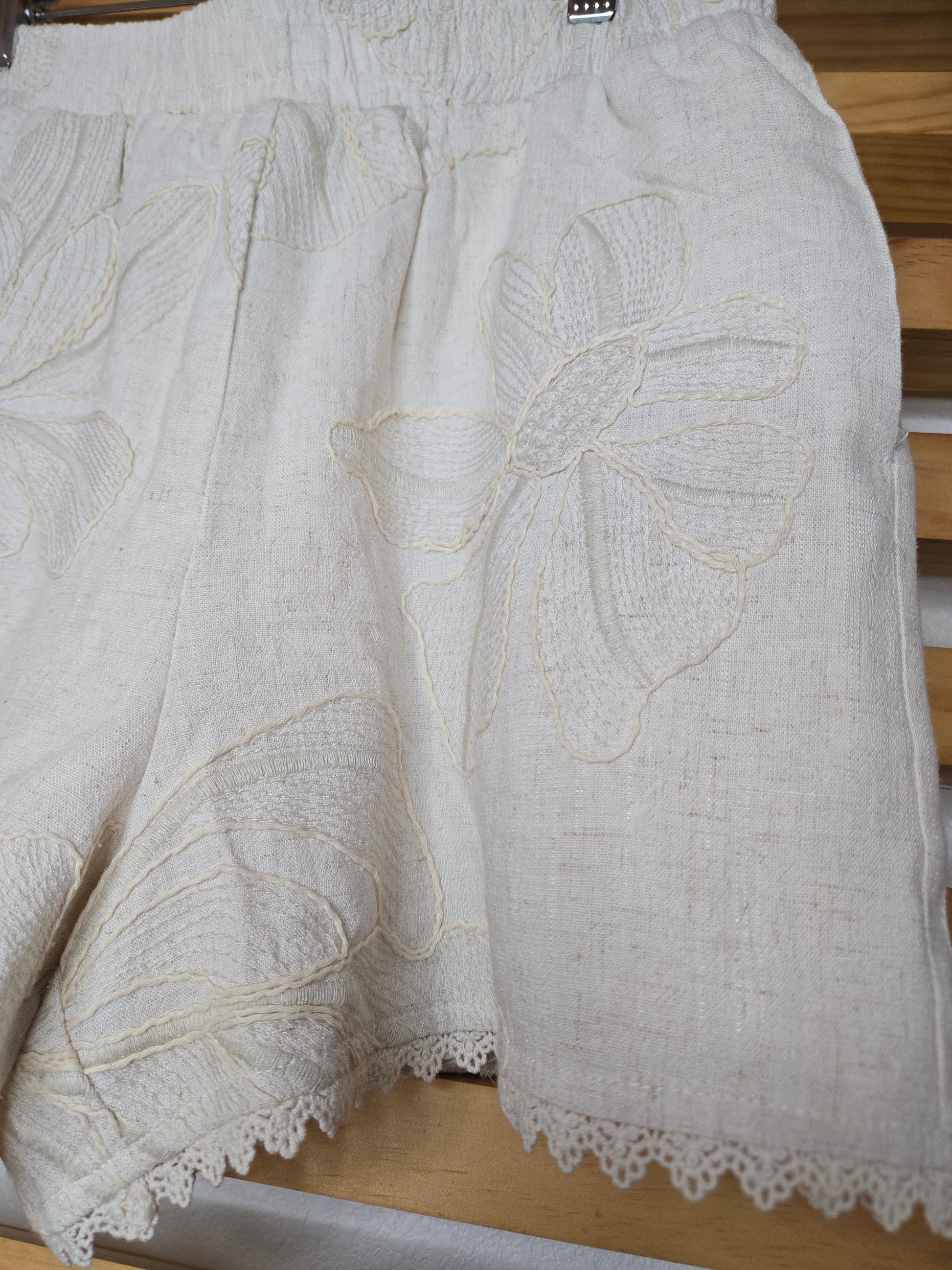 Beige embroidered shorts featuring delicate floral embroidery, crochet lace trim, side pockets, and a comfortable elastic waistband. Styled with the matching embroidered top, sold separately.