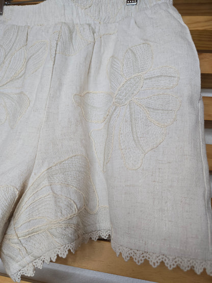 Beige embroidered shorts featuring delicate floral embroidery, crochet lace trim, side pockets, and a comfortable elastic waistband. Styled with the matching embroidered top, sold separately.