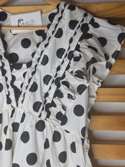 Black and white polka dot babydoll blouse with ruffle details, fitted bust, relaxed lower silhouette, and side zipper.