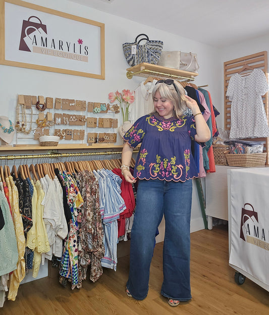 Woman wearing a navy short sleeve blouse with colorful embroidery details and scalloped trim accents in pink and green.