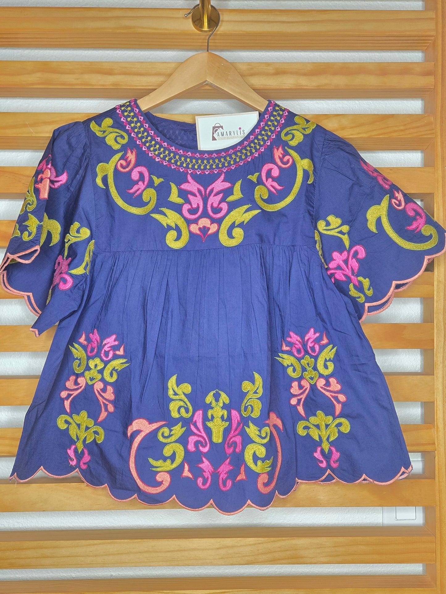 Blue dress with colorful embroidery on a wooden hanger against a wooden door background