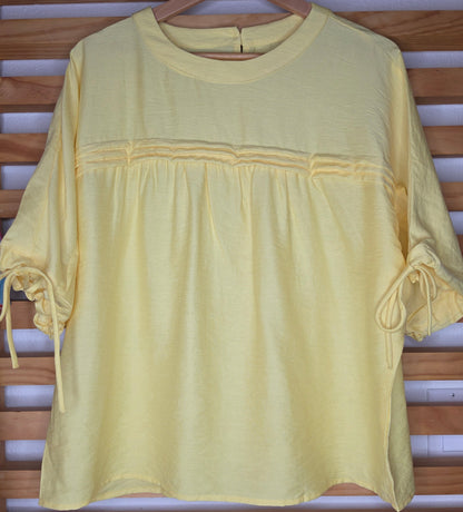 Yellow women's blouse with a round neckline, pleated details, short sleeves, and adjustable tie cuffs.