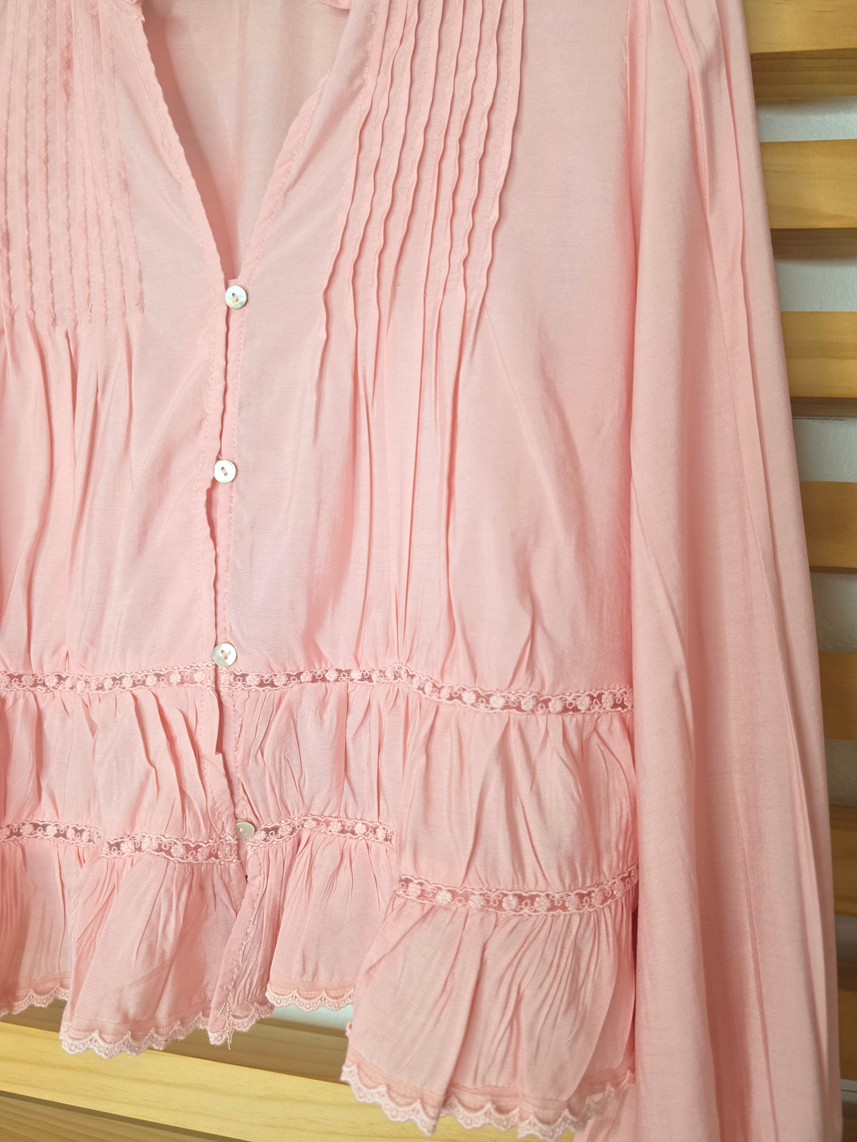 Women’s pink blouse with V-neckline, button front, lace-trimmed ruffles, delicate pin-tuck details, and long balloon sleeves with elastic cuffs.