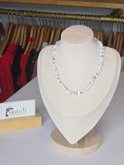 A delicate white beaded necklace with clear faceted beads displayed on a beige jewelry bust. The bust is set against a background showing clothing racks and a small sign with the brand name 'MARVIS'.
