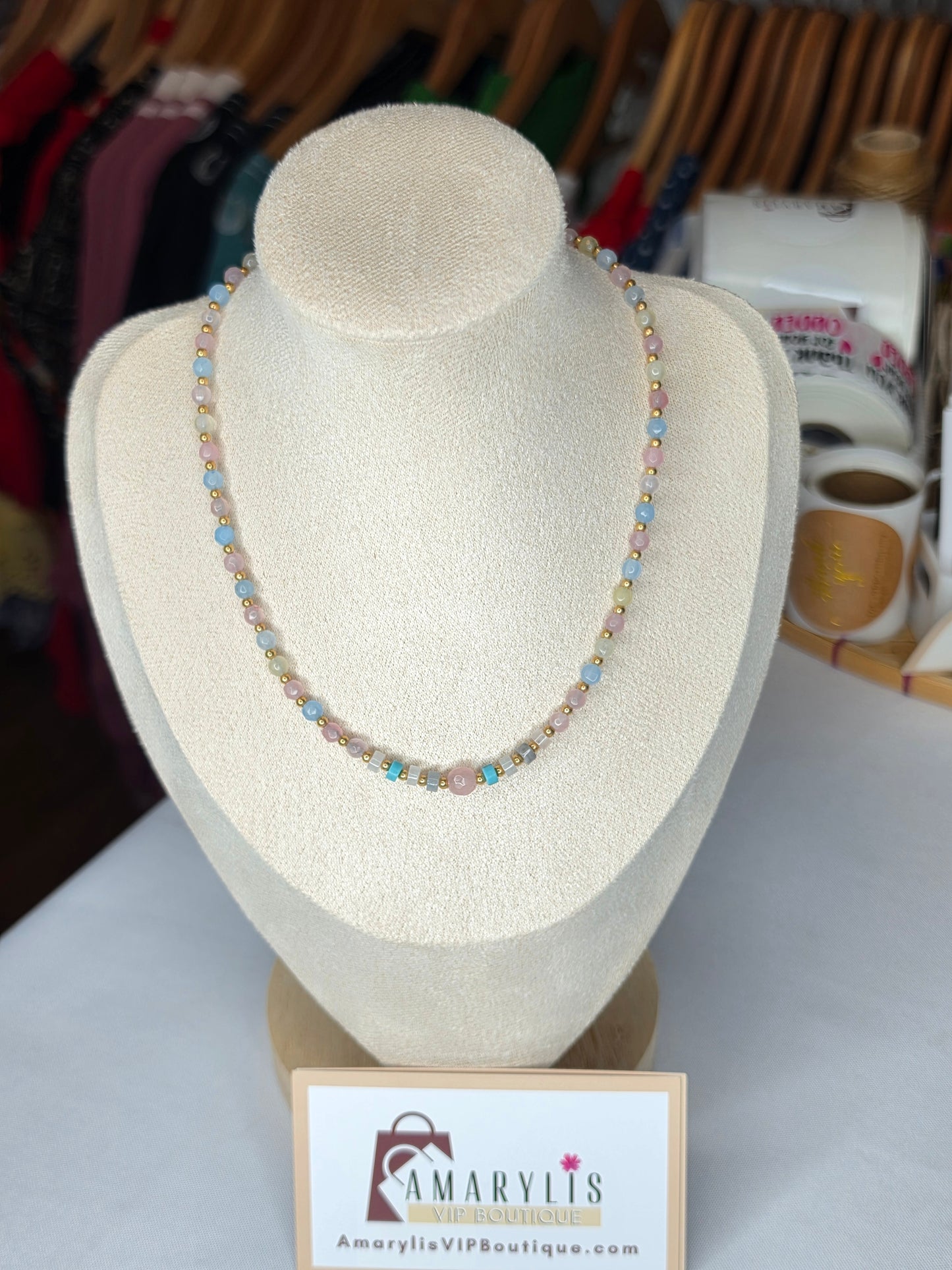 A beaded necklace displayed on a cream-colored jewelry bust. The necklace features small, round beads in pastel shades of pink, blue, yellow, and green.
