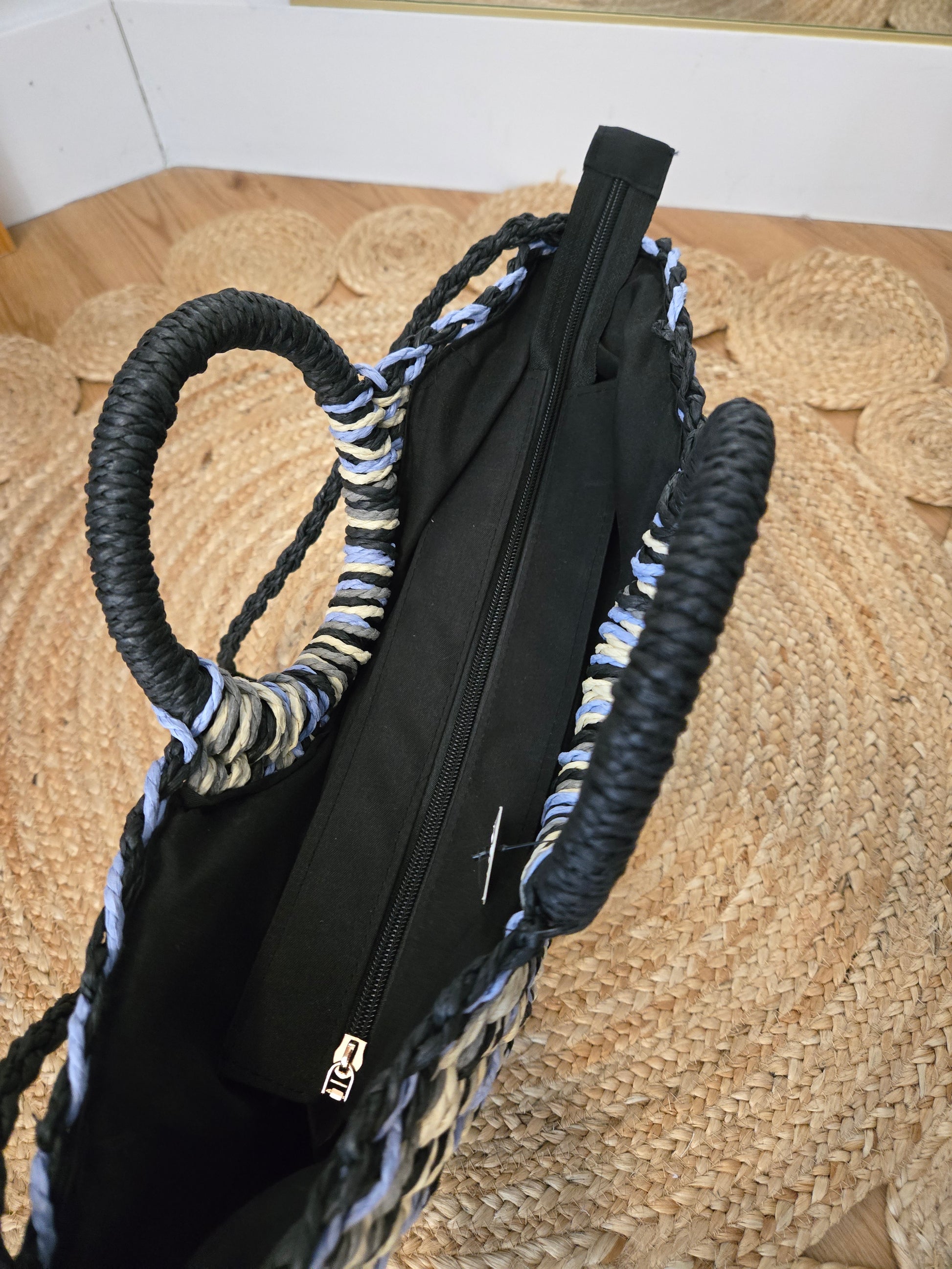 Straw tote bag with a subtle sheen, featuring a multi-tone woven design, distinctive half-moon round handles, a secure zipper closure, and an adjustable strap for crossbody wear. A versatile, timeless piece with a refined yet relaxed style.